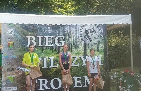 Zwycięska trójka na podium, a w tle plakat Bieg Wilczym Tropem